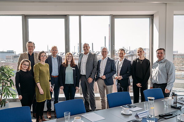 Teamfoto vor großen Fenstern mit Industrieansicht Gruppenfoto in einem modernen Büro