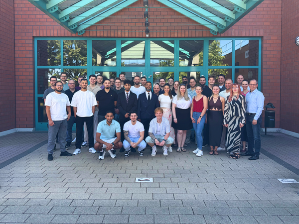 Gruppenfoto von Absolventinnen und Absolventen vor einem Backsteingebäude mit Glasdach. Die Gruppe hat ihre Fortbildung zum Industriemeister Chemie oder Pharmazie erfolgreich abgeschlossen.
