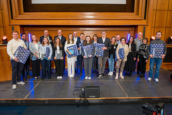 Preisverleihung: Gruppenfoto der Gewinner und Teilnehmer. Gruppe mit Preisen auf der Bühne.