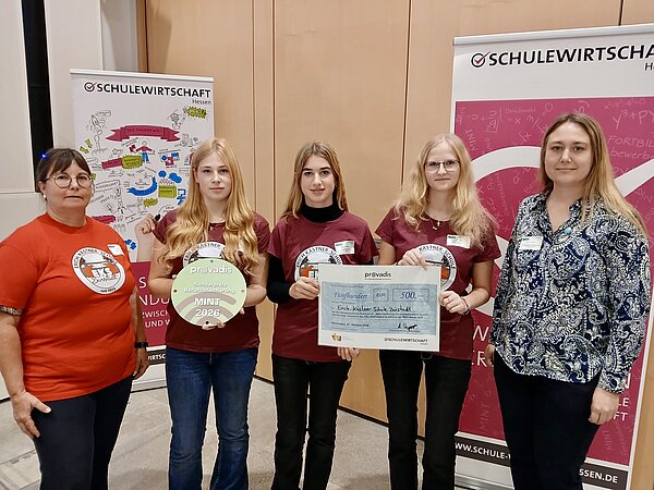 Schülergruppenfoto mit Preisverleihung und Scheck. Drei Schülerinnen der Erich-Kästner-Schule Bürstadt präsentieren gemeinsam mit zwei Begleiterinnen den Provadis-Sonderpreis Berufsorientierung MINT 2026. Sie halten eine Auszeichnungsplakette und einen symbolischen Scheck über 500 Euro in den Händen. Im Hintergrund stehen Roll-ups von SCHULEWIRTSCHAFT Hessen.