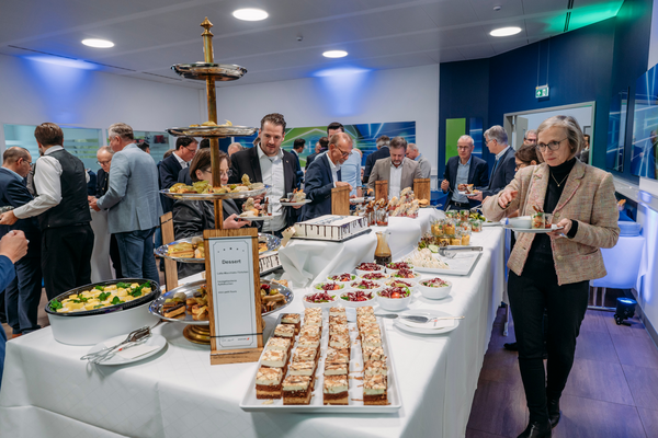 Austausch in entspannter Atmosphäre  Tisch mit Dessertbuffet und Snacks, umgeben von Personen in Business-Kleidung, die sich unterhalten und Speisen nehmen.