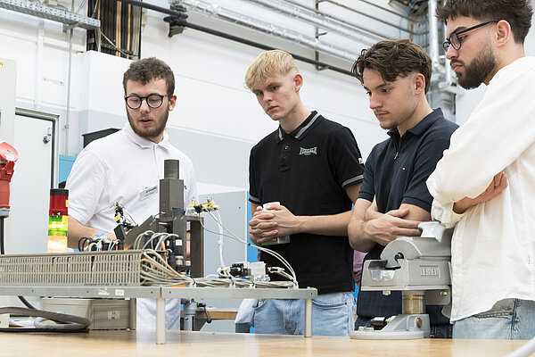 Vier junge Männer beobachten technische Demonstration. Vier junge Männer beobachten die Vorführung einer pneumatischen Übungsanlage in einer Ausbildungswerkstatt.