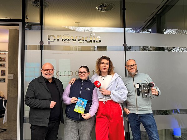 Gruppenfoto vor dem provadis Gebäude mit einer Broschüre. Vier Personen vor einem Gebäude.