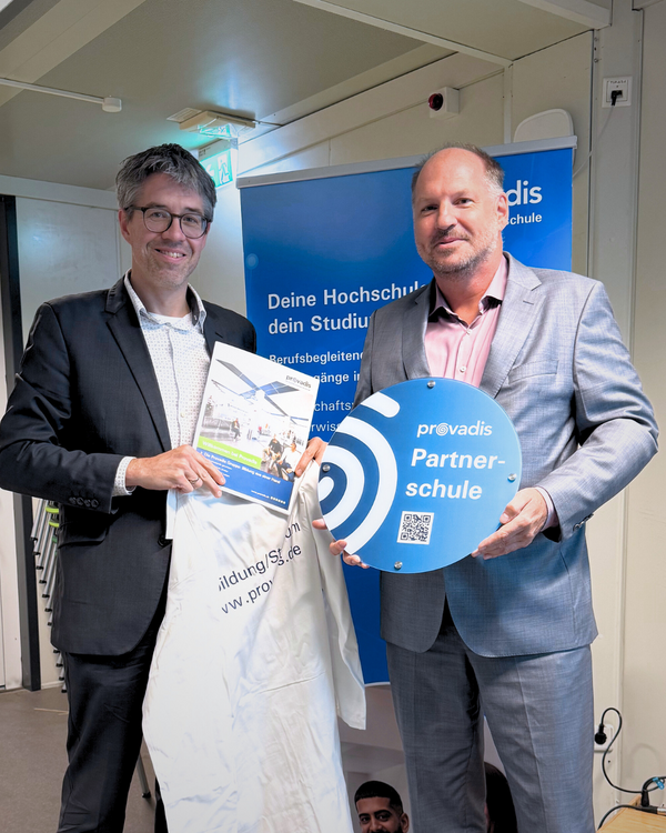 Gymnasium Süd-Schulleiter Thomas Strauch mit Provadis Hochschulvorstand Prof. Dr. Björn Hekman bei der Kittel- und Plakettenübergabe Prof. Björn Hekman, Hochschulvorstand der Provadis Hochschule, hält ein Schild mit der Aufschrift „Provadis Partnerschule“. Neben ihm steht eine weitere Person mit einem Dokument und einer Tasche. Im Hintergrund ist ein blaues Provadis-Banner zu sehen. Anlass ist die Vertragsunterzeichnung: Das Gymnasium Süd wird offizielle Partnerschule der Provadis Hochschule.
