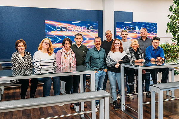 Gruppenfoto der Teilnehmenden und Projektbeteiligten der TrAB-Inhouse-Schulung bei Infraserv Höchst, die gemeinsam in einem modernen Raum stehen und lächeln, im Hintergrund sind Bildschirme mit der Aufschrift „Provadis Forum“ zu sehen.