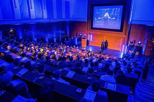 Konzert mit Publikum in einem modernen Saal Frau auf Bühne in blauer Beleuchtung