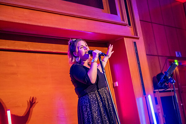 Eine Frau mit Mikrofon singt bei einer Veranstaltung. Frau singt auf einer Bühne.