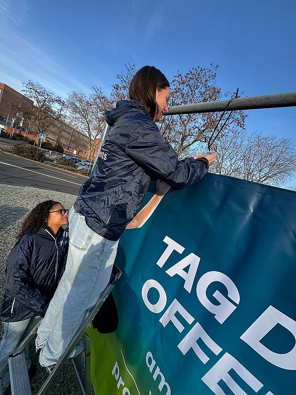 Zwei Personen montieren ein Werbebanner im Freien. Zwei Personen bringen ein Banner an.