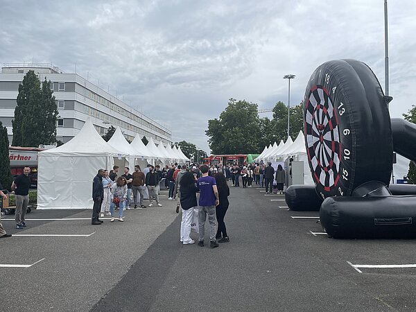 Belebter Markt mit Essensständen und Dartspiel. Markt mit Zelten und Bullseye-Dartboard.