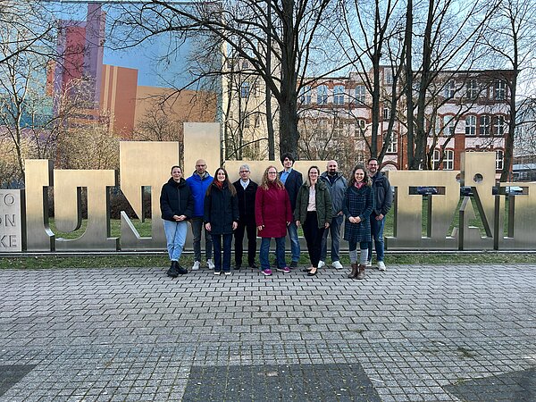Menschen stehen vor einem Kunst- und Bildungsschild Gruppe von Menschen vor einem Schild
