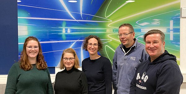 Fünf Personen posieren vor einem grafischen Hintergrund. Gruppe von fünf Personen vor einem bunten Hintergrund.